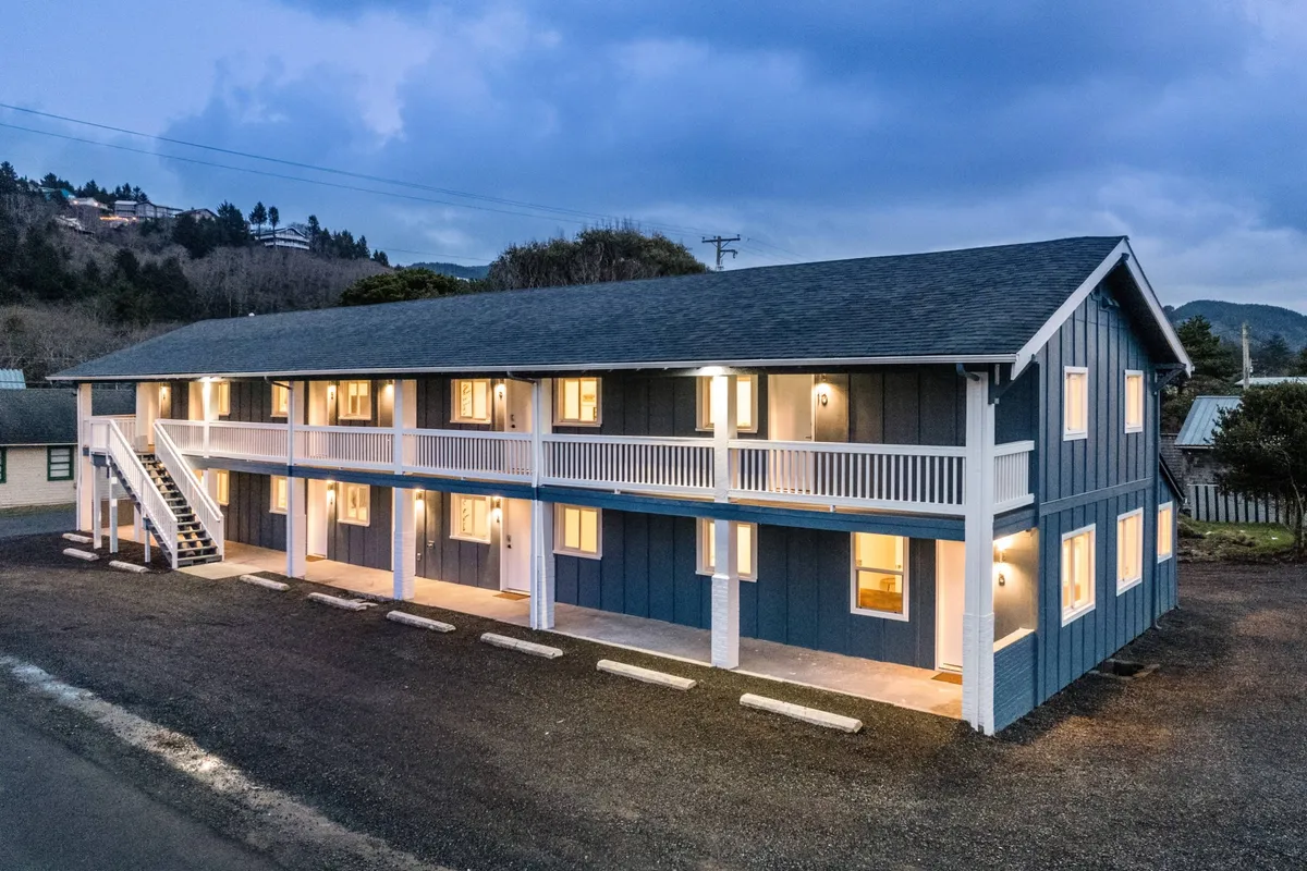 The building facade of The Inn at Rockaway Beach, warmly lit from inside, with visible balconies and staircases. The cozy lighting and inviting atmosphere hint at the comfort within, while the exterior suggests easy access to the outdoors—perfect for pet walks.