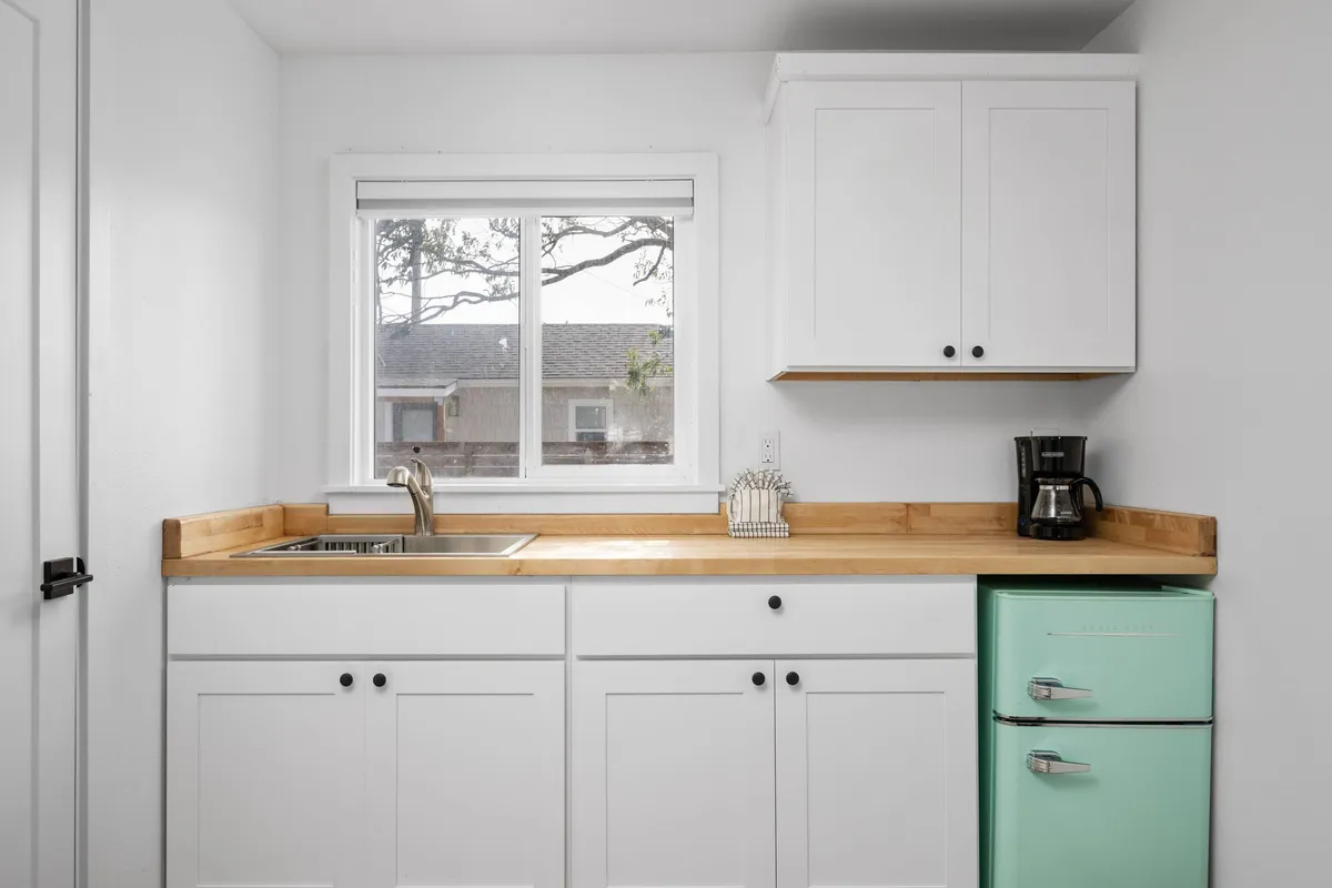 This cheerful interior scene features a mint green refrigerator, a kitchen sink, and a window letting in plenty of daylight. The space is designed for both cooking and casual dining, with a relaxed atmosphere that invites guests to enjoy their time, whether making a light meal or simply unwinding with a drink.
