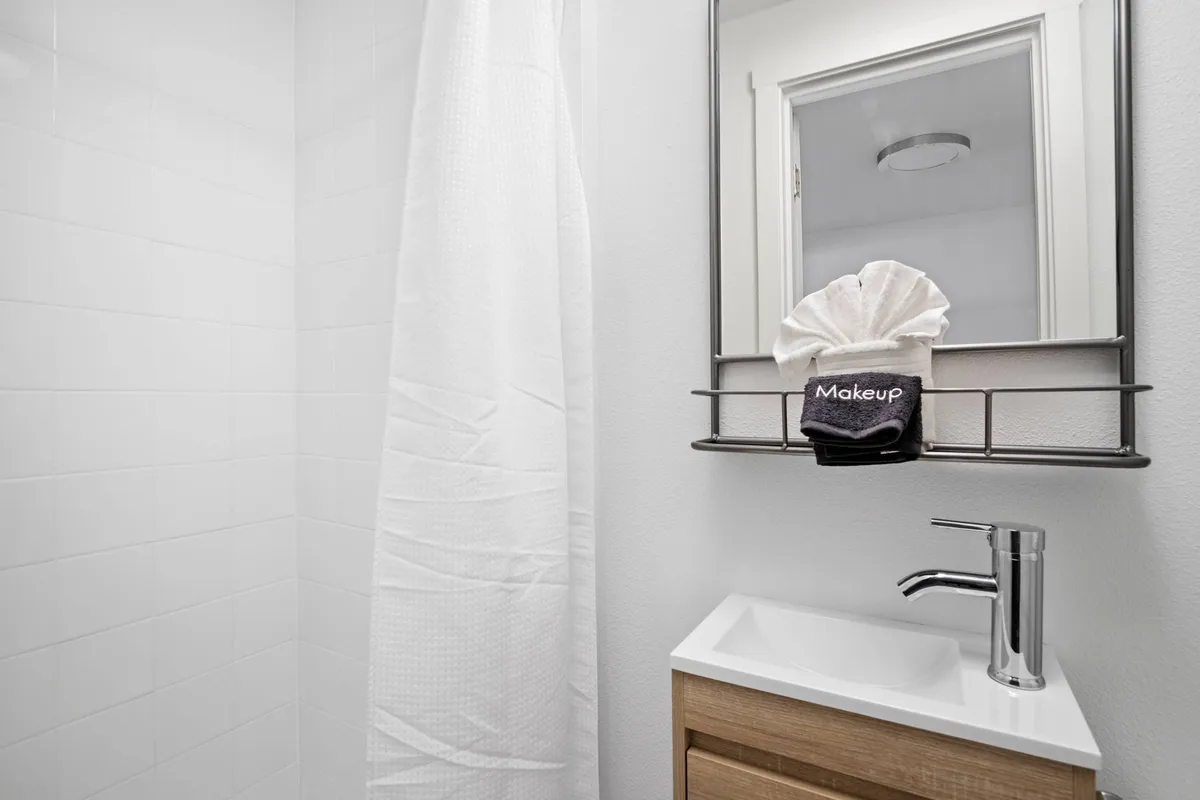 A bright, inviting bathroom featuring a modern sink, a mirror with soft lighting, a labeled 'Makeup' towel, and a patterned shower curtain. The layout suggests thoughtful attention to detail and guest comfort, emphasizing cleanliness and relaxation.