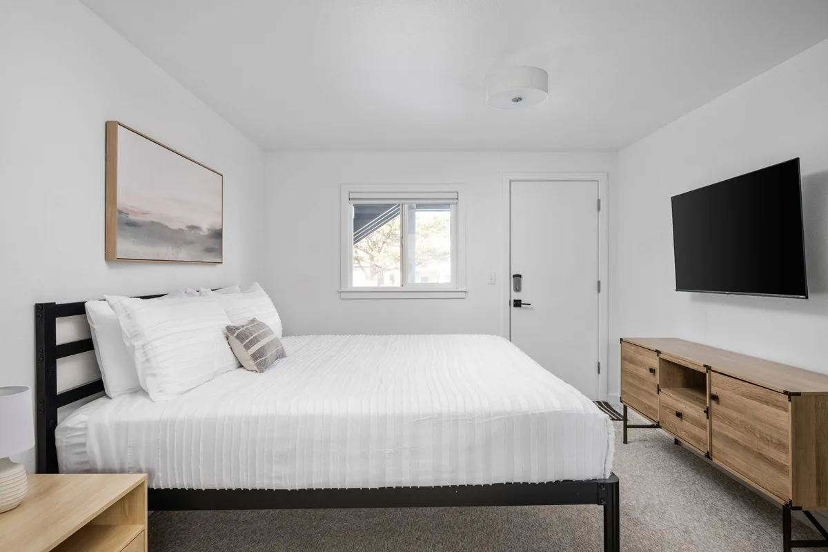 A serene bedroom scene with a comfortable bed, a dresser, window, TV, and tasteful coastal artwork. The space is bathed in soft natural light, creating a relaxing atmosphere perfect for unwinding after a day of adventure.