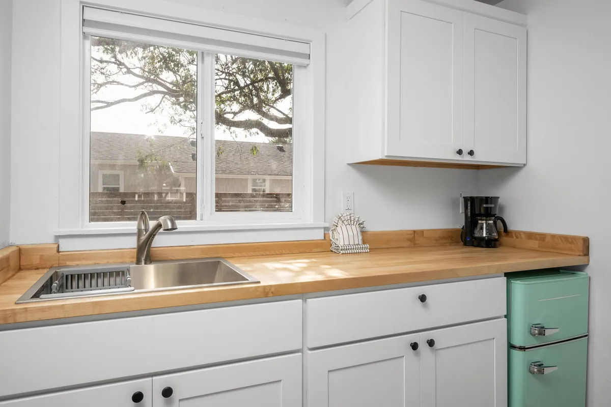 A cozy and functional kitchenette is pictured, centered on a kitchen sink with a window above for natural light. There's a colorful refrigerator and a coffee maker on the counter, suggesting that guests can easily prepare breakfast or a quick snack. The overall vibe is warm and homey, with personal touches and a layout that supports daily routines and casual dining.